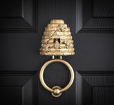 Beehive brass door knocker on a black panelled door, a straw skep with cast bees on it and a round ring below.