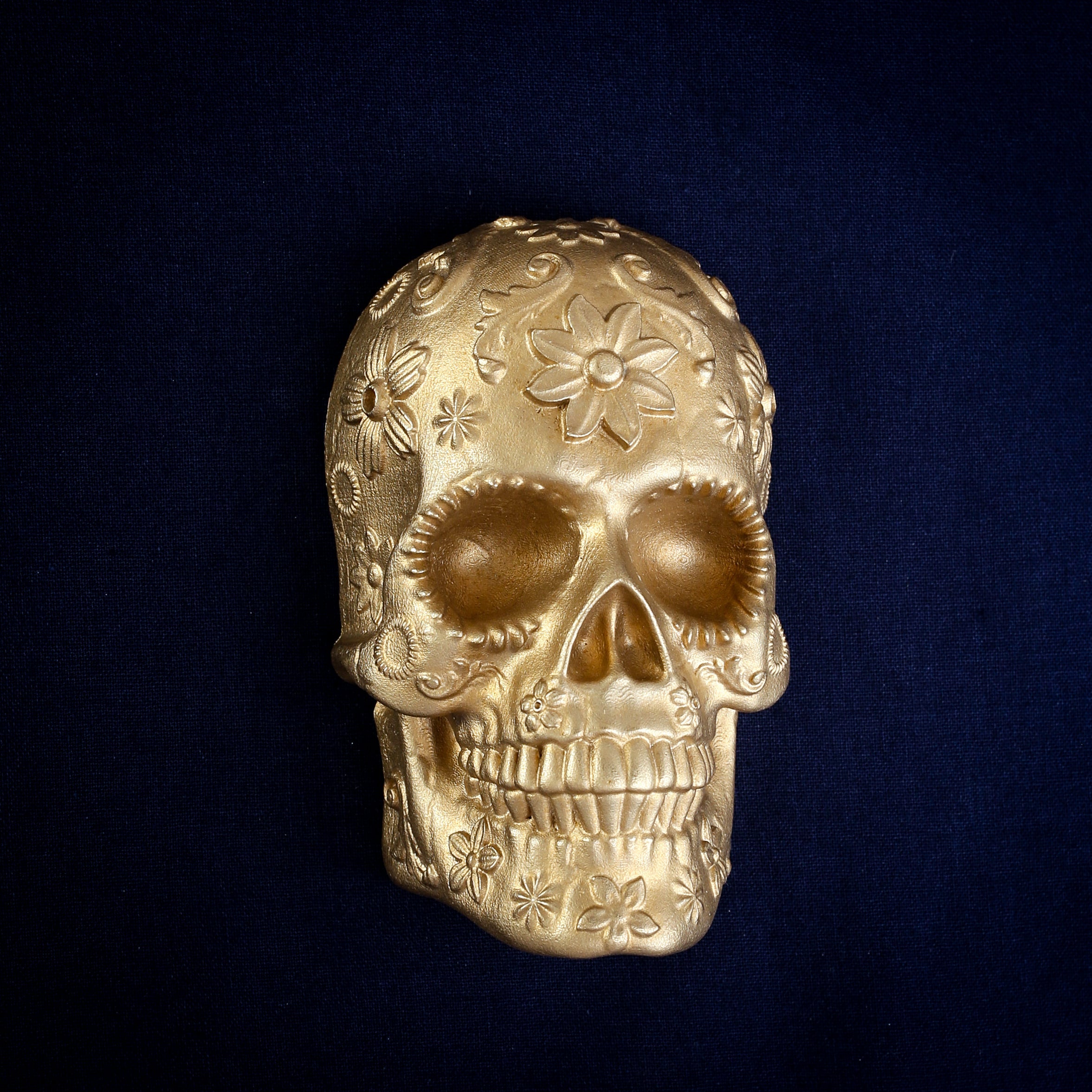 Marigold Sugar Skull interchangeable door knocker head on navy, front view, a flower on the brow and open eye sockets