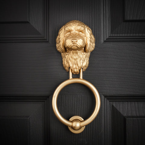 Cockapoo brass door knocker fitted to a black front door, straight on