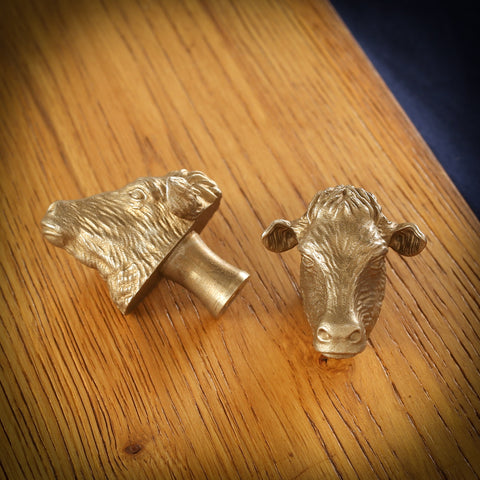 Dairy Cow brass cabinet knob and coat hook on an oak board, one on its side showing the stem, one facing front