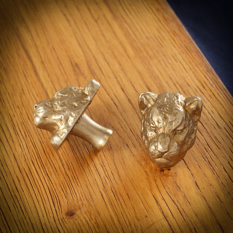 Leopard brass cabinet knob and coat hook on an oak board, one on its side showing the stem, one facing front