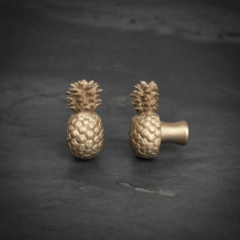 Pineapple brass cabinet knob and coat hook on dark slate, one facing front, one turned side on showing the stem