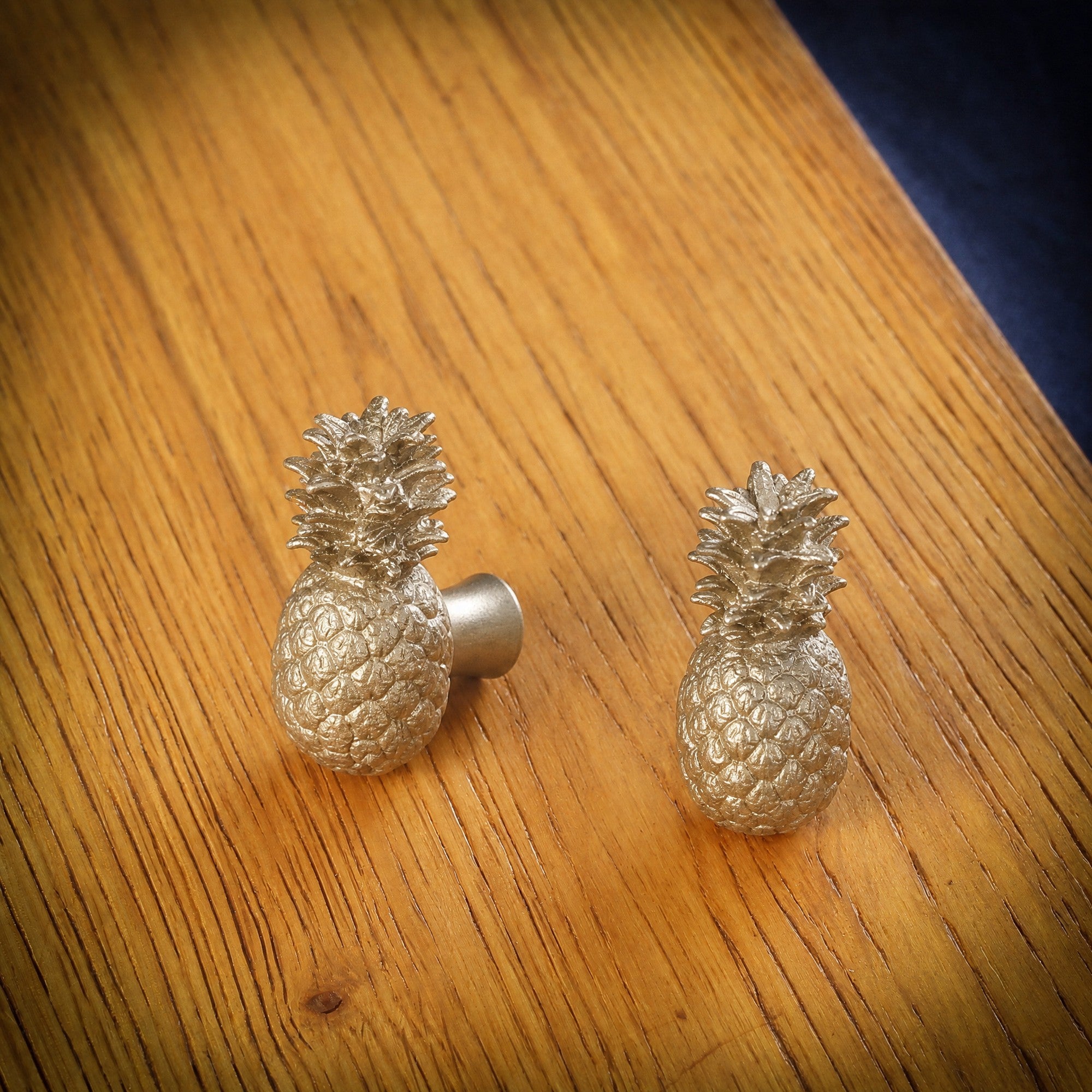 Pineapple brass cabinet knob and coat hook on an oak board, one turned to show the stem, one facing front