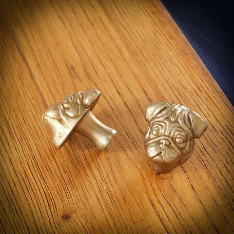 Pug brass cabinet knob and coat hook on an oak board, one on its side showing the stem, one facing front