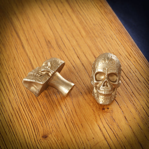Sugar Skull brass cabinet knob and coat hook on an oak board, one front on with scrollwork on the brow, one on its side