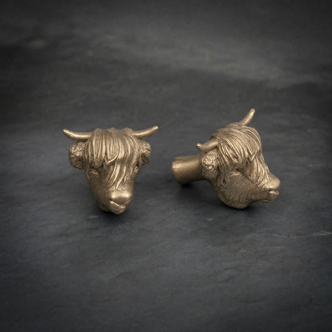 Highland Cow brass cabinet knob and coat hook with its tongue out, on dark slate, one facing front, one side on showing the stem