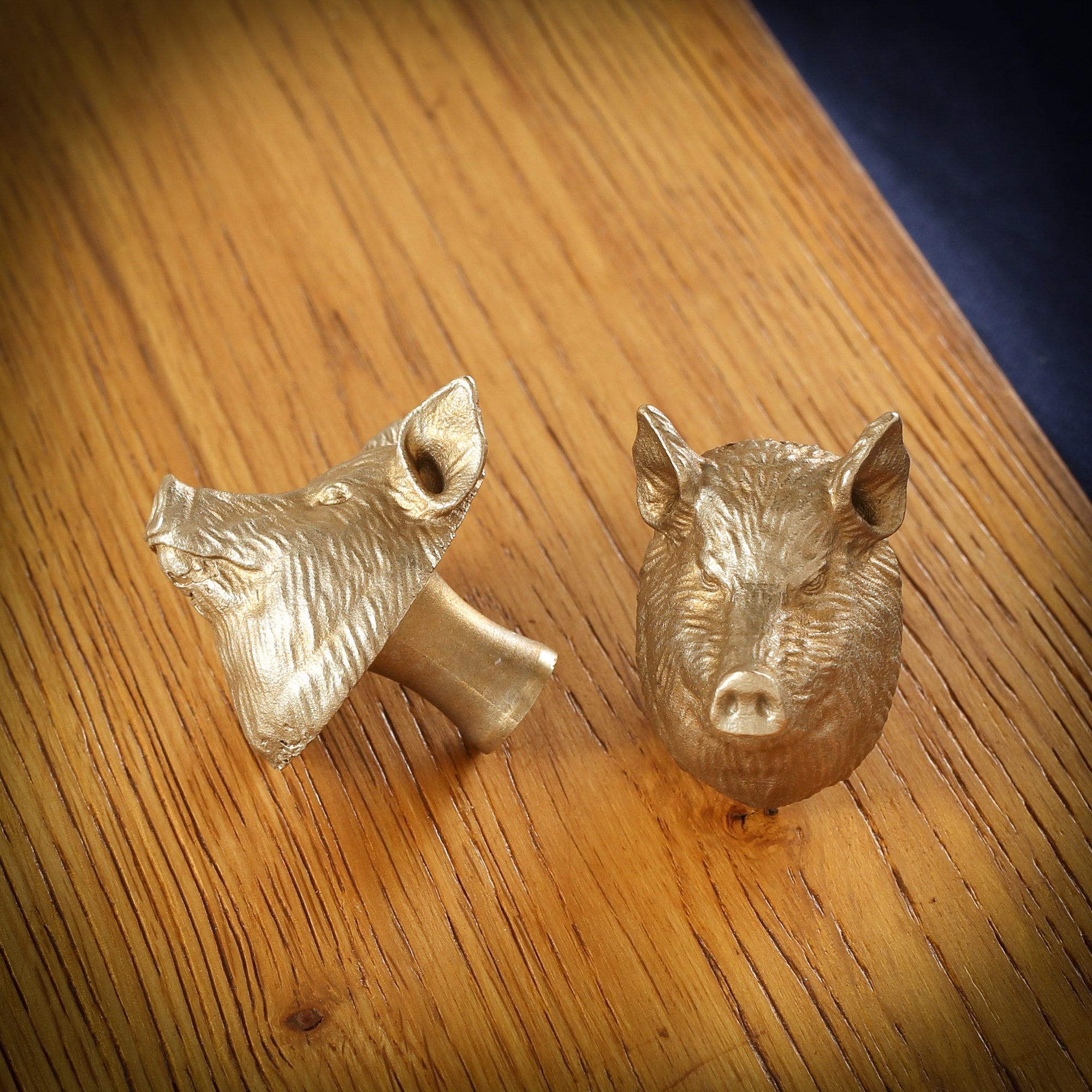 Yorkshire Pig brass cabinet knob and coat hook on an oak board, one on its side showing the stem, one facing front